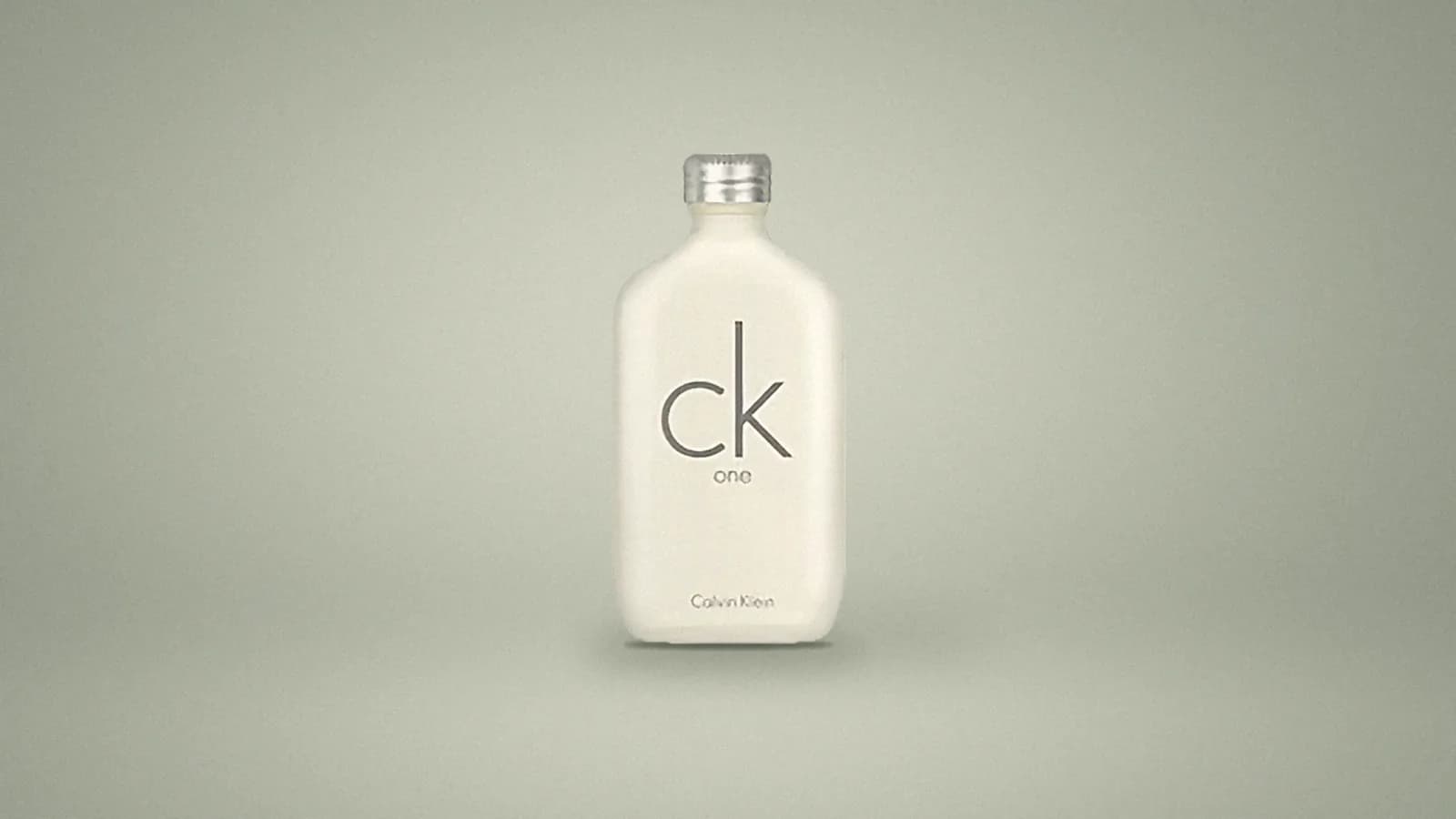 Our photo of the CK One bottle, a frosted flask with a silver screw cap, standing on a soft sage-grey studio backdrop