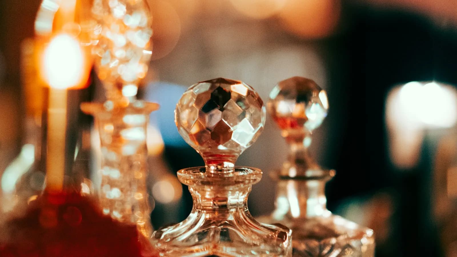 Cut-crystal perfume bottles with faceted stoppers, lit warmly from behind on a dressing table