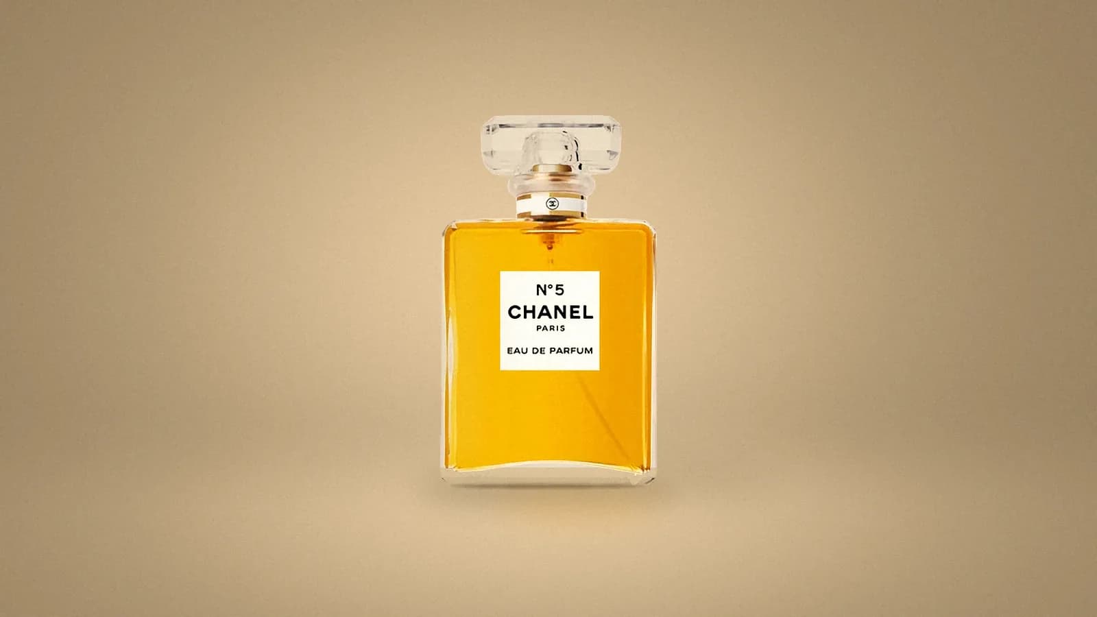 Our catalogue photo of a Chanel N°5 Eau de Parfum bottle, a clear rectangular flacon of gold perfume with a white label and a faceted glass stopper, set on a soft champagne backdrop