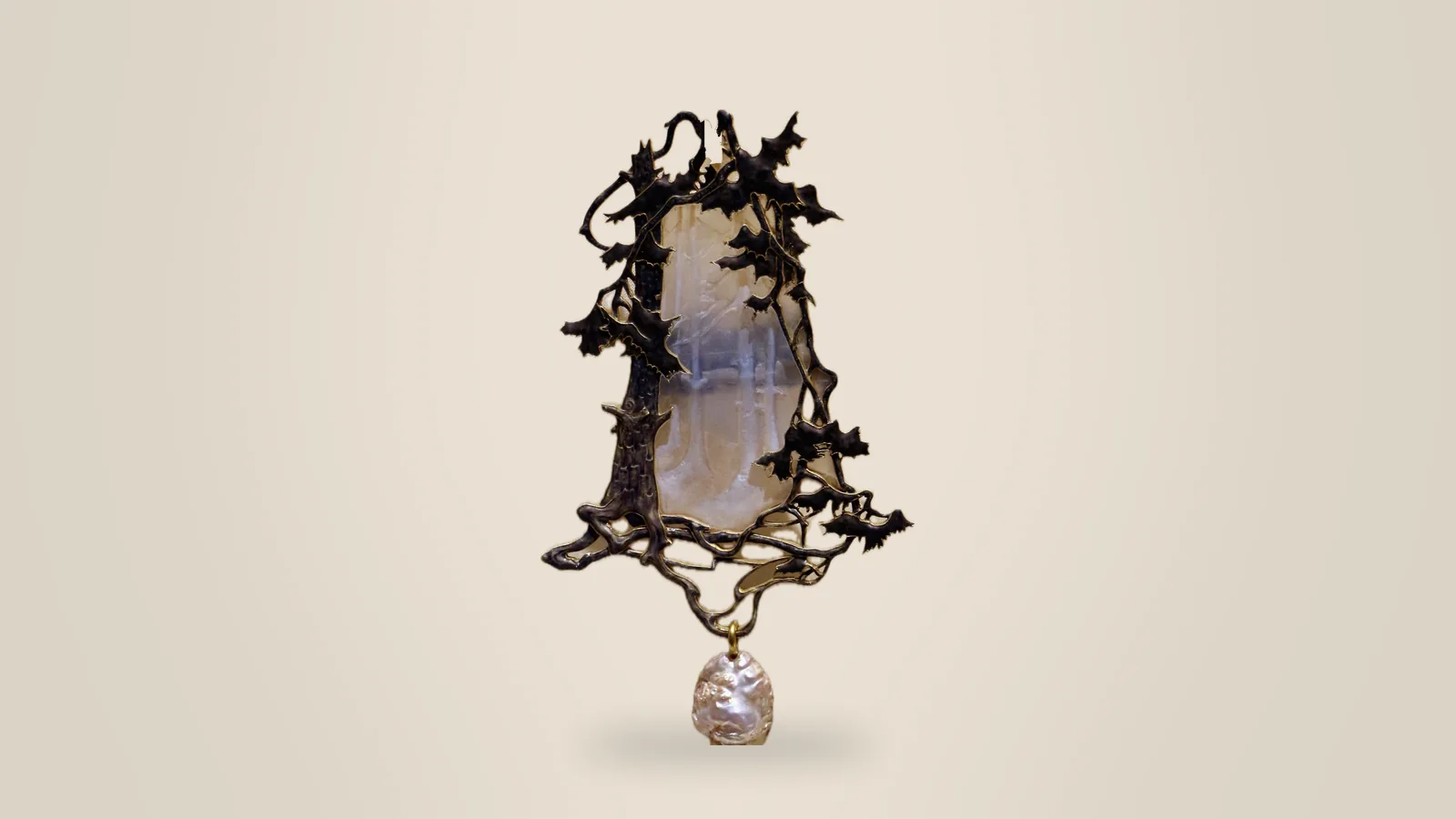 A René Lalique forest pendant in glass and metal on a pale backdrop